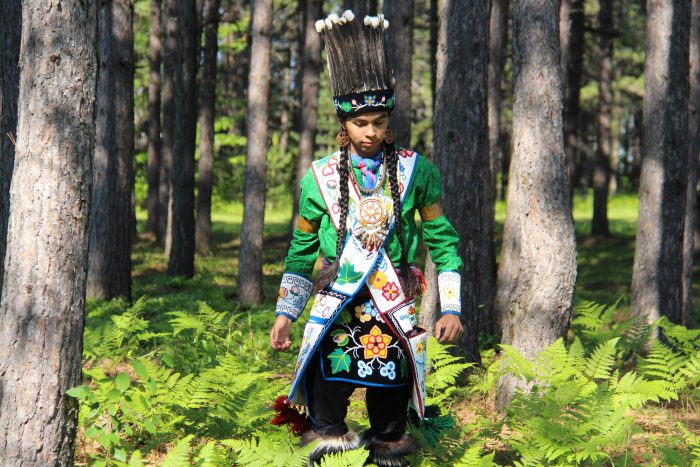 student in woodland regalia standing outside in forest