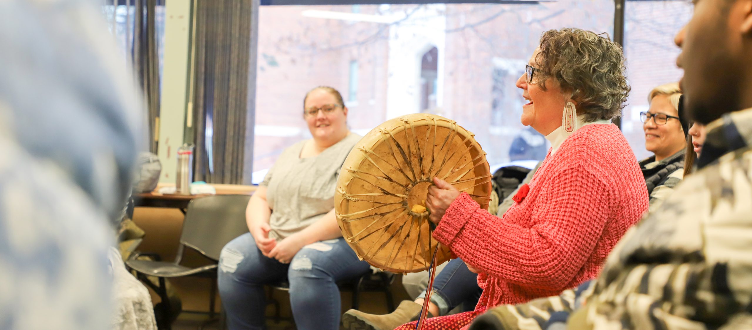 professor playing traditional Anishinaabe drum while class sit in circle